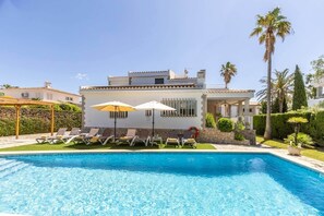 En moderne villa med swimmingpool, liggestole og parasoller.