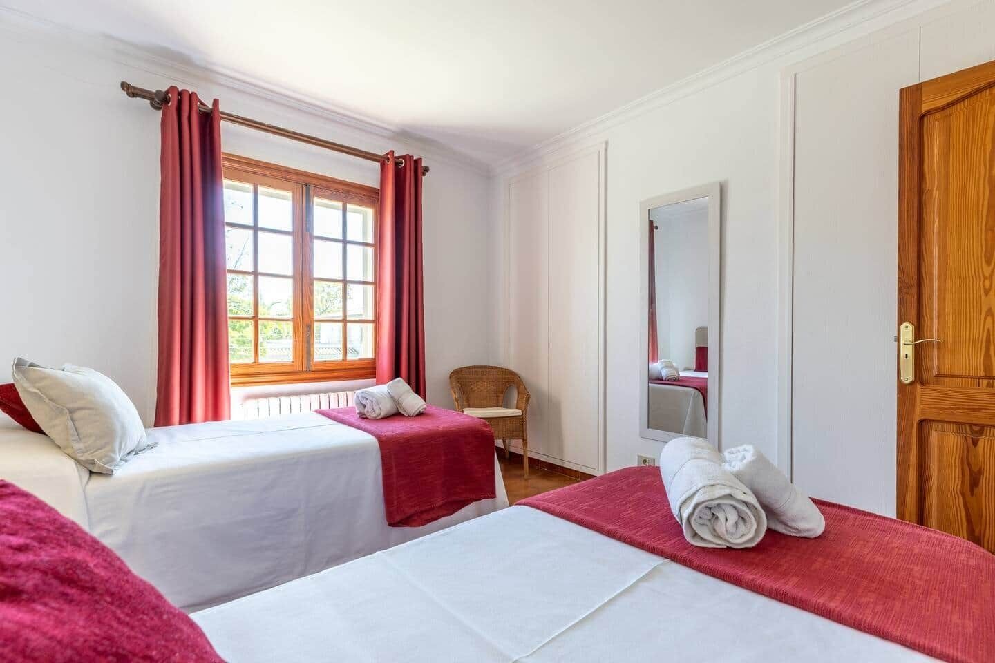 Une chambre d’hôtel avec deux lits, une fenêtre avec des rideaux, une chaise, un miroir et une porte en bois.