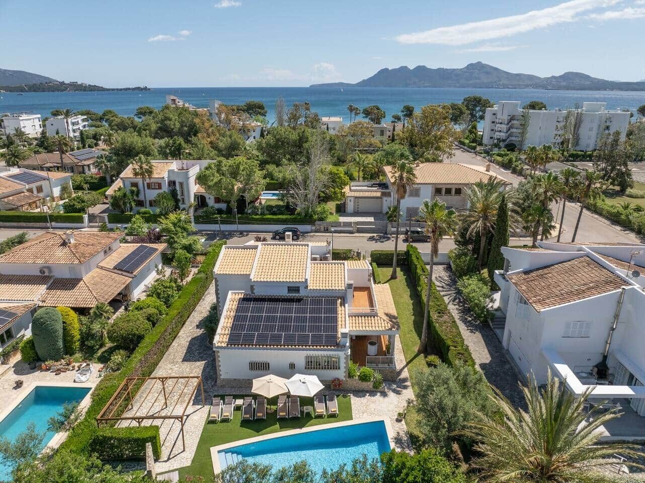 A residential area with a swimming pool, solar panels, and a view of the sea.