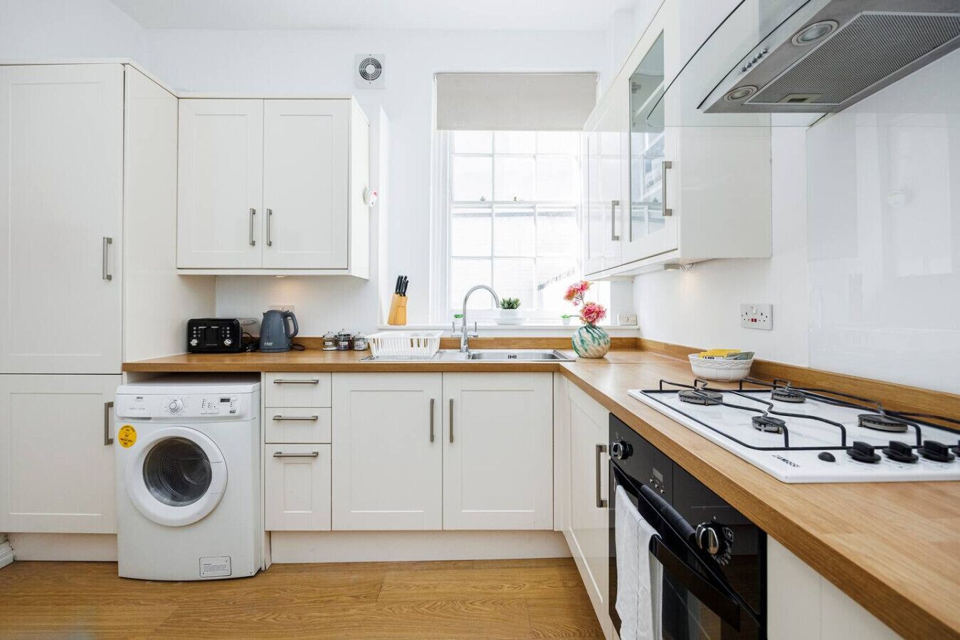 Une cuisine moderne avec des meubles blancs, un lave-linge, une cuisinière et une fenêtre.