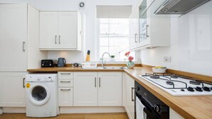 Una cocina moderna con alacenas blancas, lavadora, estufa y ventana.