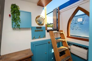 A room with a wooden ladder, a blue cabinet, a mirror, and a window with a view.