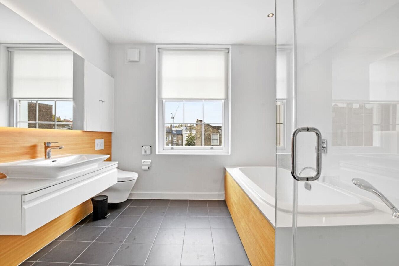 A modern bathroom with a large mirror, two sinks, a toilet, and a glass-enclosed shower.