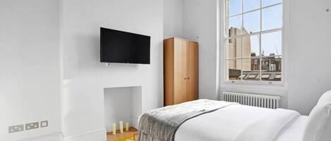 A bedroom with a bed, a TV mounted on the wall, a wardrobe, a window with a view, and a radiator.