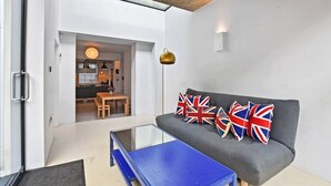 Una sala moderna con un sofá, una mesa de centro de vidrio y un área de comedor visible a través de una puerta abierta.