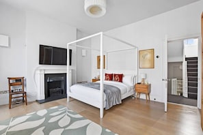 Ein Schlafzimmer mit Himmelbett, Kamin, Fernseher und einer Treppe zu einer oberen Etage.