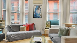 Ein Wohnzimmer mit grauem Sofa, einem Glastisch und einem Bücherregal.