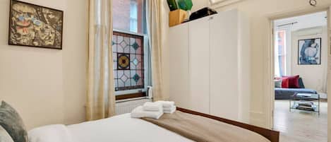 Une chambre à coucher avec un lit, une fenêtre avec des rideaux, un radiateur, une armoire et un tableau accroché au mur.