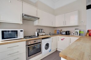 A modern kitchen with a microwave, gas stove, toaster, and washing machine. - 1 Bedroom Apartment in Central Soho - 4 people (Greater London)
