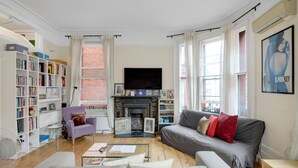 Ein Wohnzimmer mit Kamin, Sofa, Bücherregal und Fernseher.
