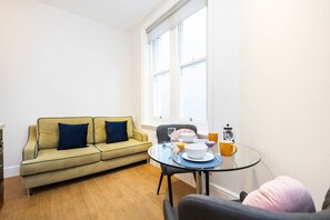 A living room with a sofa, a glass table with a bowl, and a window. - Stylish Studio in Leicester Square - 2 guests (Greater London)