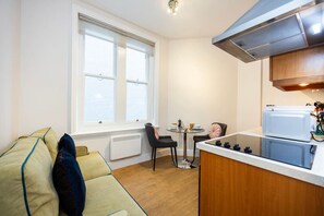 Eine kleine Küche mit Herd, einem Esstisch mit Stühlen und einem Fenster, das natürliches Licht hereinlässt.