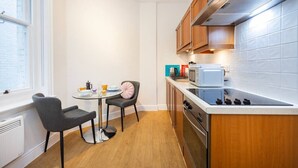 Een kleine keuken met een eettafel, stoelen, een fornuis en een raam.