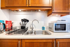 A kitchen with wooden cabinets, a stainless steel sink, a microwave, and a utensil holder. - Stylish Studio in Leicester Square - 2 guests (Greater London)