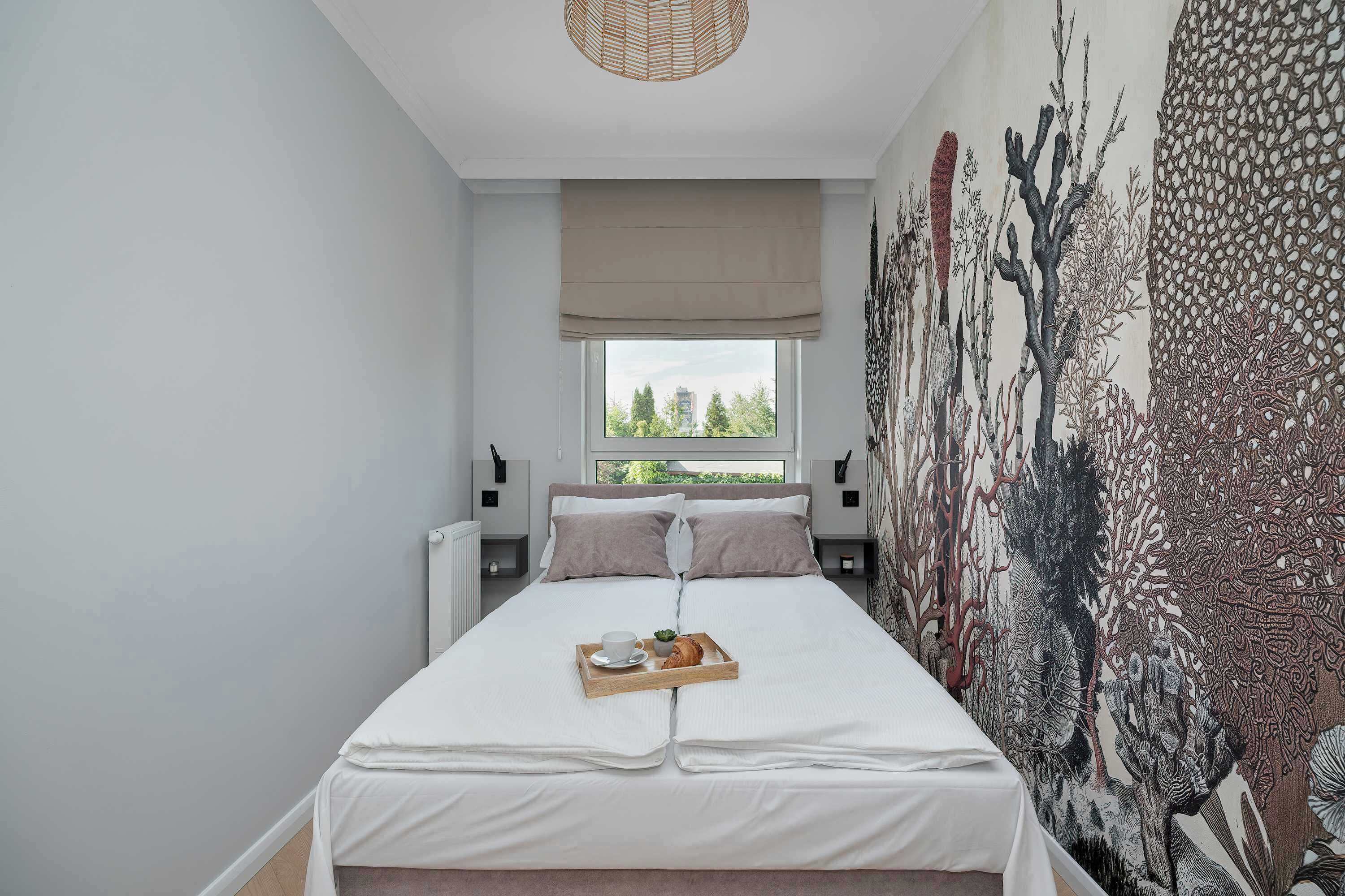 A bedroom with a bed, a window, a wall mural, and a tray with a cup and a pastry.