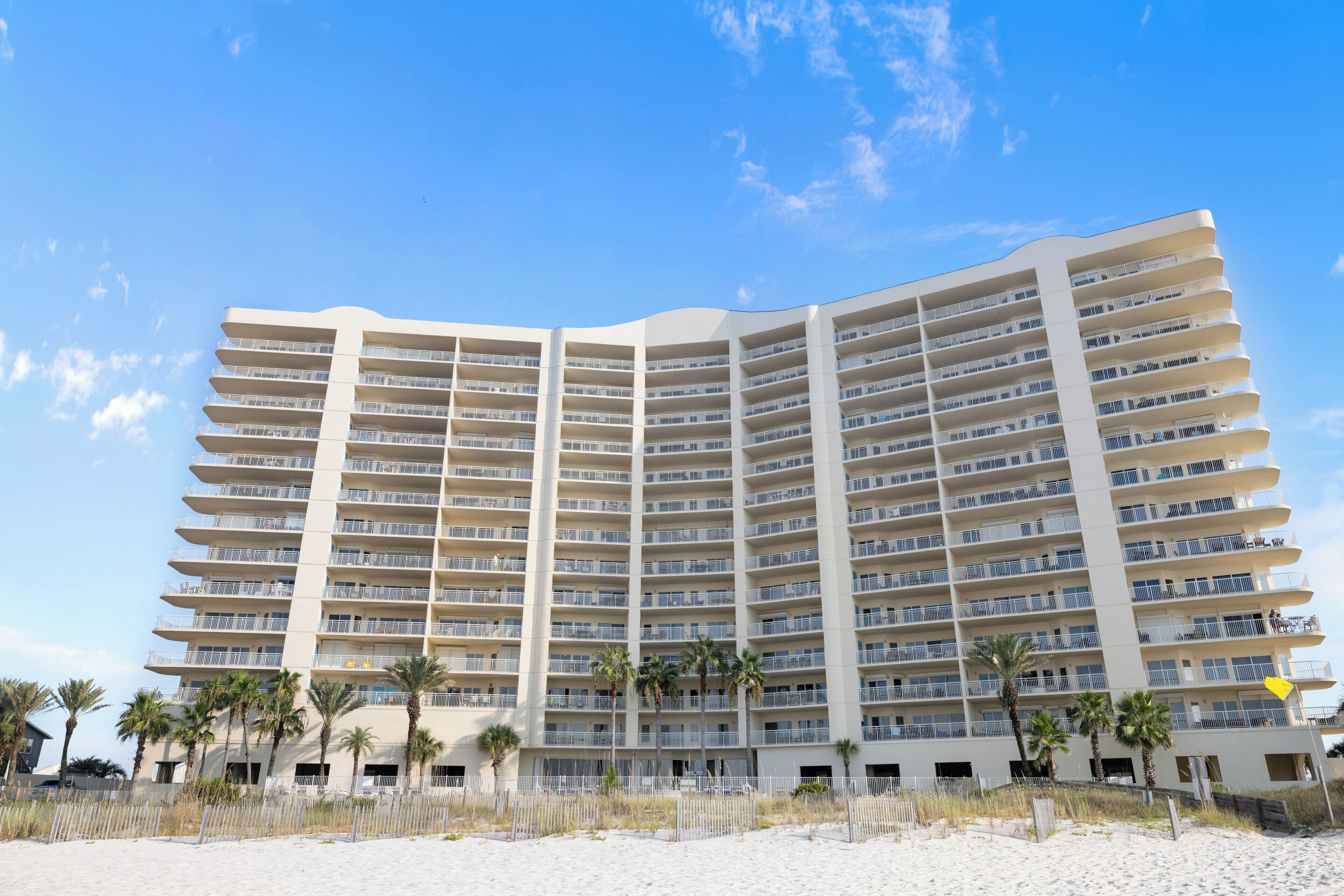 Een hotel met meerdere verdiepingen en balkons, nabij een zandstrand.