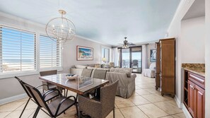 A spacious dining area with a large table and chairs, a kitchen with wooden cabinets, and a balcony with a view of the beach. - Broadmoor 701 by Liquid Life (Orange Beach)