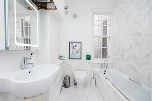 Une salle de bain avec un lavabo blanc, des toilettes, une baignoire et un tableau encadré au mur.