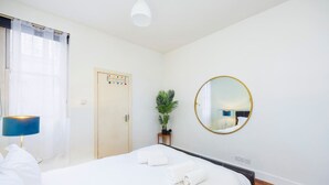 Hotellihuone, jossa on sänky, yöpöytälamppu, ruukussa oleva kasvi, pyöreä peili ja ovi, jossa on värikoodattu lukitusjärjestelmä.