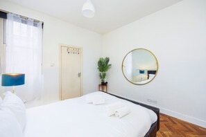 A hotel room with a bed, a bedside lamp, a potted plant, a round mirror, and a door with a color-coded lock system. - 1BR in Dean Street Central - 4 people (Greater London)