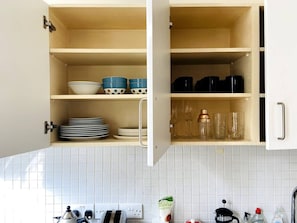 A kitchen with open cabinets displaying dishes, glasses, and a coffee maker. - 1BR in Dean Street Central - 4 people (Greater London)