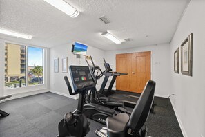 Un gimnasio con cintas de correr, una bicicleta estática y una televisión instalada en la pared.