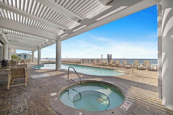 Zona de piscina techada con sillones de descanso y jacuzzi, con vista a una playa.