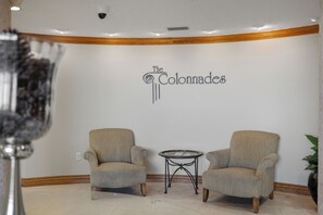 Una habitación con dos sillones, una pequeña mesa redonda y un cartel en la pared que dice 'The Colonnades'.