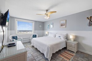 Ein Schlafzimmer mit einem Bett, einem Deckenventilator, einem Fernseher, einem Fenster und Blick auf den Strand.