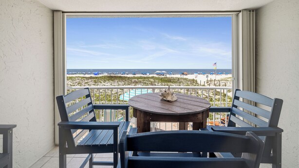 A balcony with a table and chairs, overlooking a beach with a clear sky. - Castaways 1C by Liquid Life (Gulf Shores)