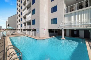 Ein Poolbereich eines Hotels mit klarem, blauem Pool, einem weißen Zaun und einem Gebäude mit Balkonen.