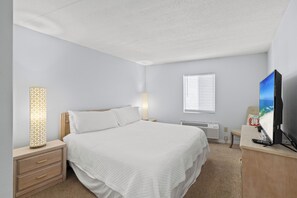 Quarto com cama, mesas de cabeceira, televisão e janela com persianas.
