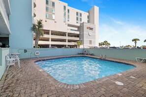 Ein Schwimmbecken mit Pflasterung, eine Palme und ein Hotelgebäude mit Parkgarage im Hintergrund.