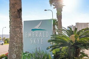 Schild für Emerald Skye mit einem Segelboot-Logo, umgeben von Palmen und Blumen.