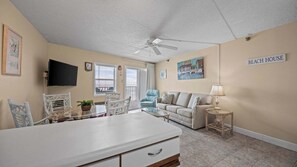 Ein Strandhaus-Interieur mit Essbereich, einer Couch, einem Fernseher und einem Deckenventilator.