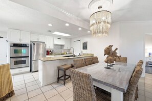 A modern kitchen with white cabinetry, stainless steel appliances, a granite countertop, and a dining area with wicker chairs and a glass table. - Four Seasons 204W by Liquid Life (Orange Beach)