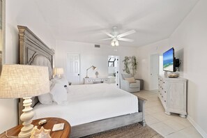 Ein Schlafzimmer mit Bett, Schreibtisch, Stuhl, Fernseher und Deckenventilator.