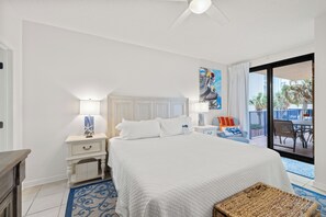 A hotel room with a large bed, a nightstand, a lamp, a painting, and a view of the outside. - Four Seasons 204W by Liquid Life (Orange Beach)