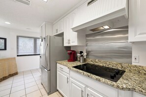 Eine moderne Küche mit weißen Schränken, einem Edelstahl-Kühlschrank, einer roten Kaffeemaschine und einer Arbeitsplatte aus Granit.