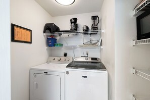 A compact laundry room with a washing machine, a dryer, and a microwave on a shelf. - Four Seasons 204W by Liquid Life (Orange Beach)