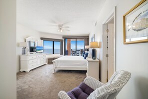 A hotel room with a bed, a desk, a chair, a ceiling fan, and a view of the ocean. - Four Seasons 702E by Liquid Life (Orange Beach)