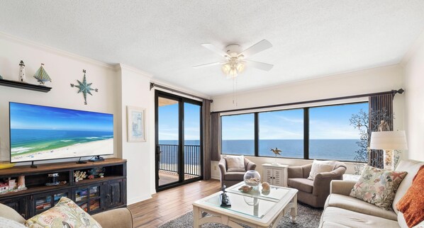 A spacious living room with a large TV, comfortable seating, a ceiling fan, and a view of the ocean. - Four Seasons 702E by Liquid Life (Orange Beach)