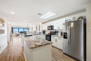 A modern kitchen with a central island, stainless steel appliances, and a view to the living area. - Four Seasons 702E by Liquid Life (Orange Beach)