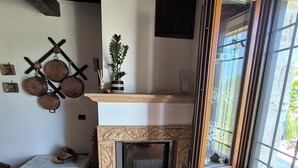 Una chimenea con macetas decorativas, una pequeña mesa con una bota y un ventanal con vistas.