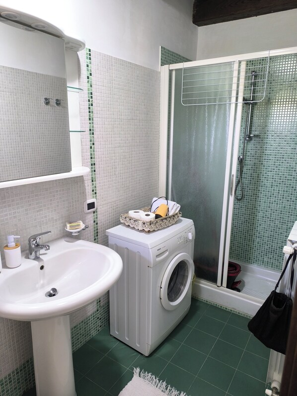 A bathroom with a sink, washing machine, and glass shower enclosure.