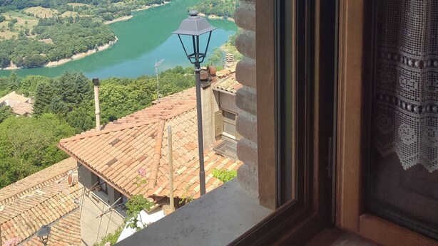 Vista a través de una ventana que muestra un río, colinas verdes y un poste de luz.