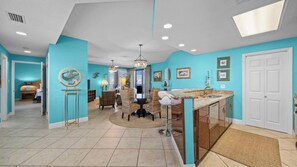 A spacious living area with a dining table, wicker chairs, and a chandelier. - Four Seasons 901W by Liquid Life (Orange Beach)