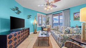 A living room with a TV, sofa, coffee table, and ceiling fan. - Four Seasons 901W by Liquid Life (Orange Beach)