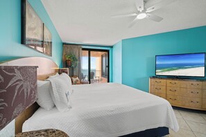 Ett hotellrum med en säng, en tv, en takfläkt och utsikt över stranden.