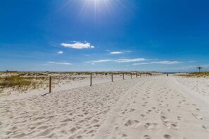 Ein Weg durch den Sandstrand, mit Fußabdrücken, einem klaren Himmel und vereinzelter Vegetation.